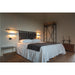 Bedroom with upholstered headboard, white bedding, dark throw, metal side table, and wood storage chest.