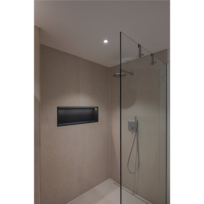 Modern shower with glass door, recessed black niche, and beige stone tile.