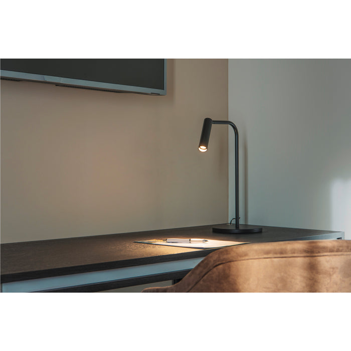 Black metal desk lamp with a gooseneck design, illuminating a paper and pen on a dark surface.