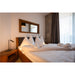 Bedroom with wood bed frame, white linens, wood nightstand, and wood-framed mirror.