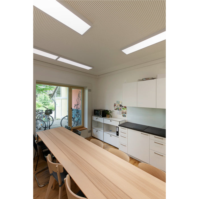 Modern office kitchen with light wood table, white cabinets, black countertop, and recessed lighting.