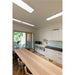Modern office kitchen with light wood table, white cabinets, black countertop, and recessed lighting.