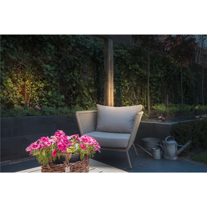 Wicker outdoor chair with gray cushion, pink petunias in basket, and copper finish garden lights.