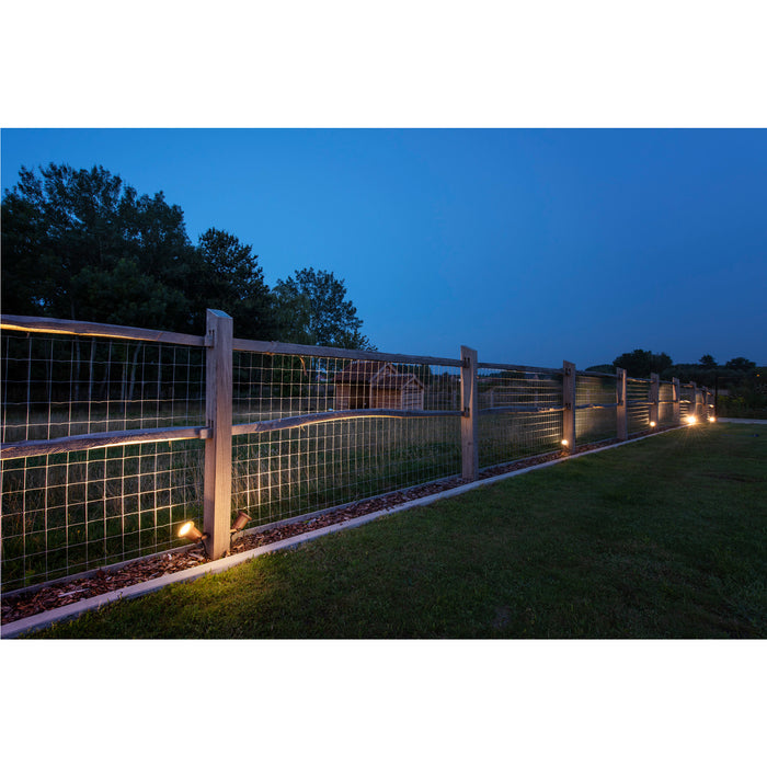 Wooden fence with wire mesh and warm-toned spotlights illuminating a yard at dusk.