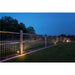 Wooden fence with wire mesh and warm-toned spotlights illuminating a yard at dusk.