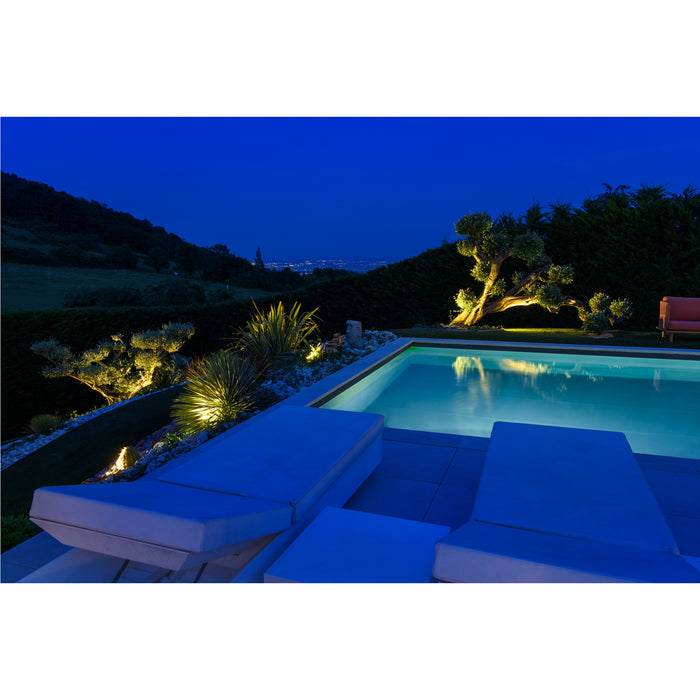 Modern pool with white lounge chairs, stone patio, and landscape lighting at night.
