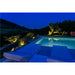 Modern pool with white lounge chairs, stone patio, and landscape lighting at night.