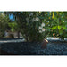 Bronze finish landscape spotlight, ground mounted among gray gravel and greenery.