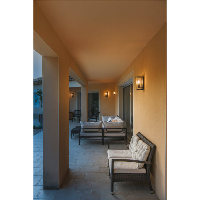 Outdoor patio with wicker furniture, white cushions, and black metal wall-mounted lights.