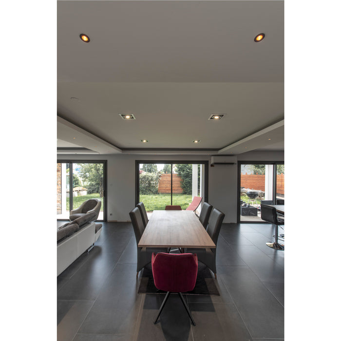 Modern dining room with wood table, gray leather chairs, and red velvet accent chair on dark tile floor.