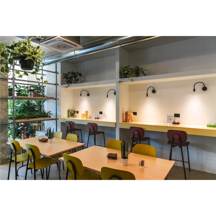 Modern cafe interior with light wood tables, yellow and burgundy chairs, and wall-mounted black sconces.