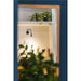 Interior view through a blue frame: plants on a shelf, a black wall-mounted lamp, and decorative ceramic vases.