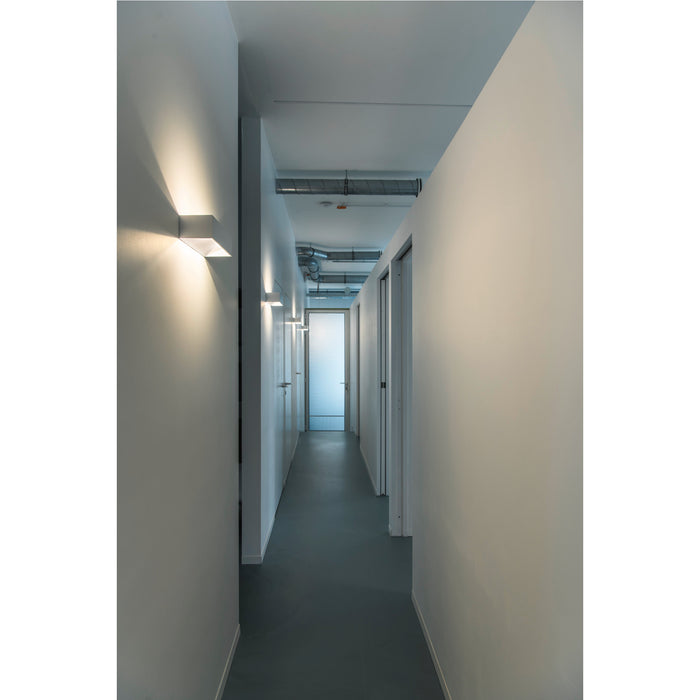 Hallway with white walls and gray floor, featuring square white wall-mounted sconces.