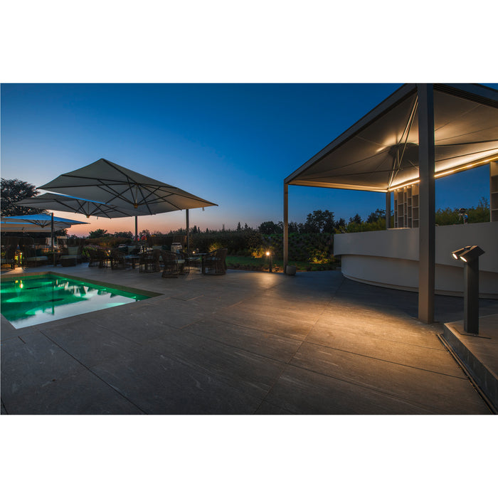 Outdoor patio with dark gray stone pavers, pool, umbrellas, and ground lights at dusk.