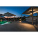 Outdoor patio with dark gray stone pavers, pool, umbrellas, and ground lights at dusk.