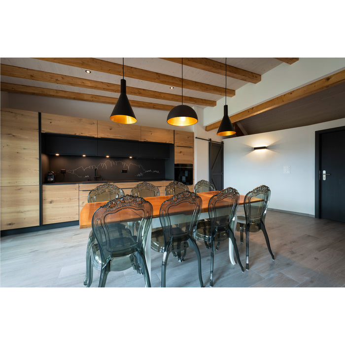 Dining room with wood table, smoke-tinted acrylic chairs, and black pendant lights with gold interiors.