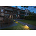 Black rectangular path light illuminating a stone and grass walkway in front of brick buildings.