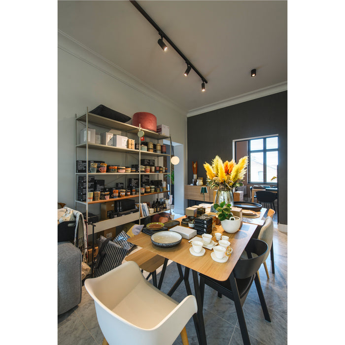 Interior view of a retail space with a light wood table set with ceramic tableware and a metal shelving unit displaying various products.