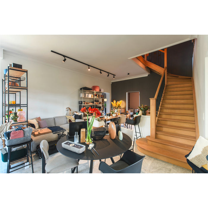 Modern living room interior with black round dining table, wood staircase, gray sofa, and metal shelving.