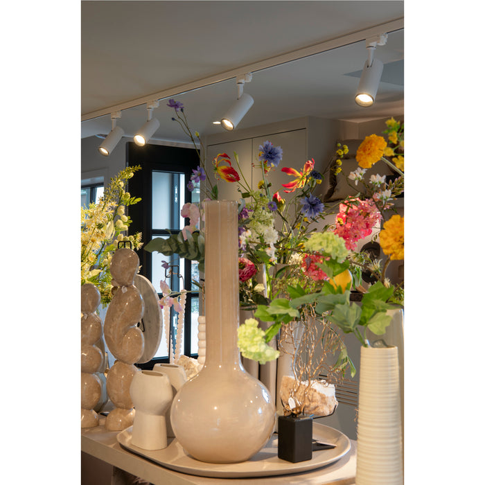 Ceramic vases in beige and white with glossy finish, displayed with colorful flowers and track lighting.