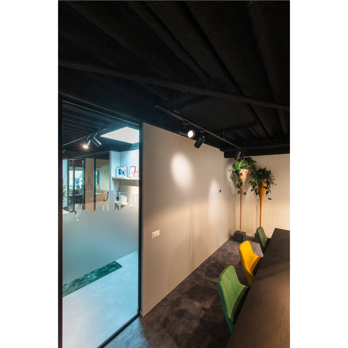 Office interior with black ceiling, track lighting, frosted glass door, and green/yellow upholstered chairs.