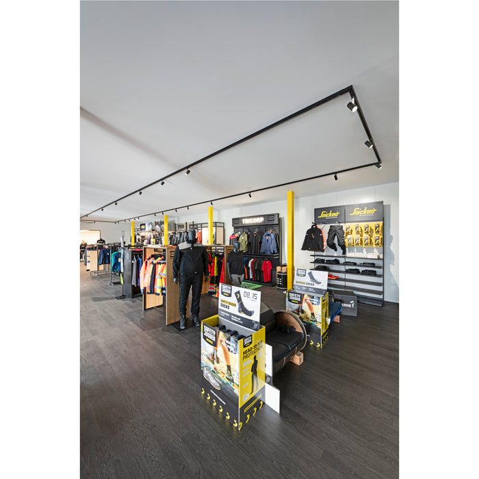 Retail store interior with workwear clothing displays, black track lighting, and dark wood-look flooring.
