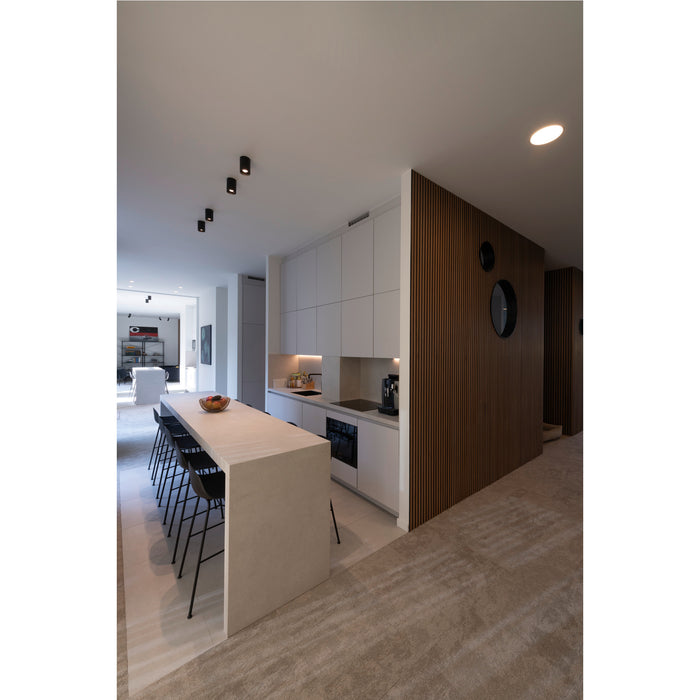 Modern kitchen with white cabinets, light countertop, black bar stools, and wood slat wall.