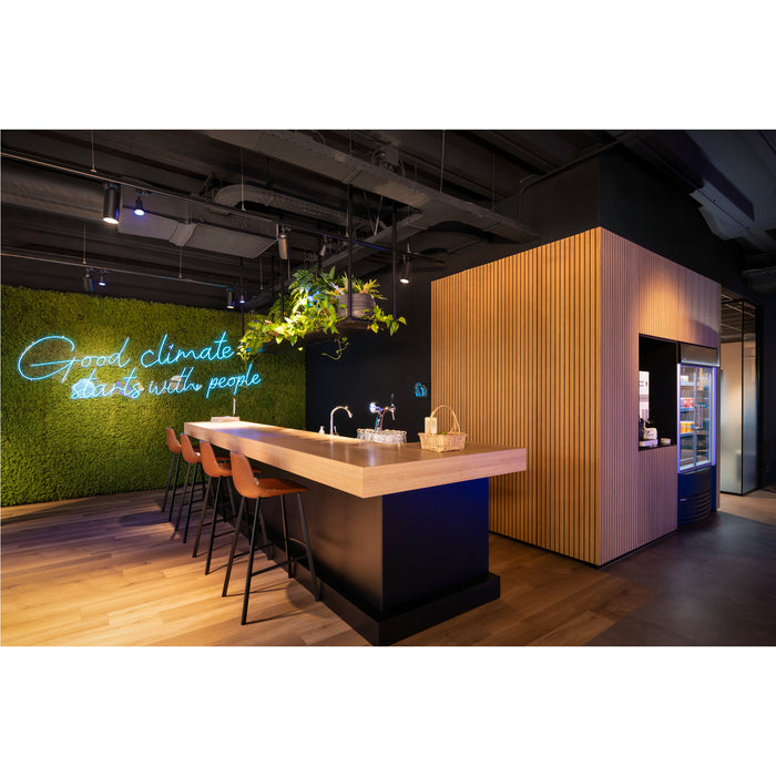 Office break room with wood bar, brown leather stools, moss wall with neon sign, and wood-paneled vending machine area.