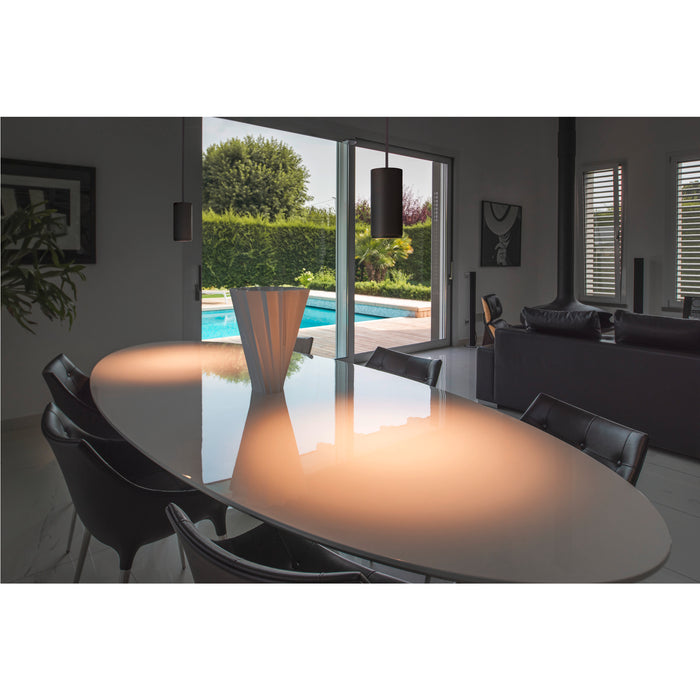 Modern dining room with oval table, black leather chairs, and cylindrical pendant lights.