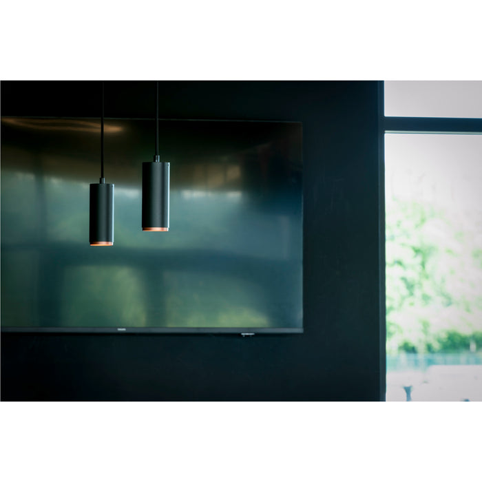 Two black cylinder pendant lights, metal with copper accents, hanging in a modern interior.