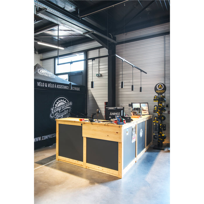 Bike shop interior with a light wood and gray reception desk, black pendant lights, and Auvray security products display.