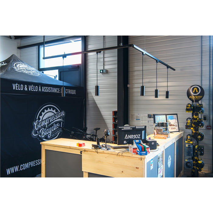 Bike shop interior with a light wood counter, black pendant lights, and a black tent with "Compression Bicycles" logo.