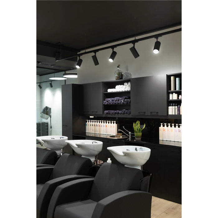 Modern hair salon interior with black cabinets, track lighting, and white ceramic shampoo bowls with black chairs.