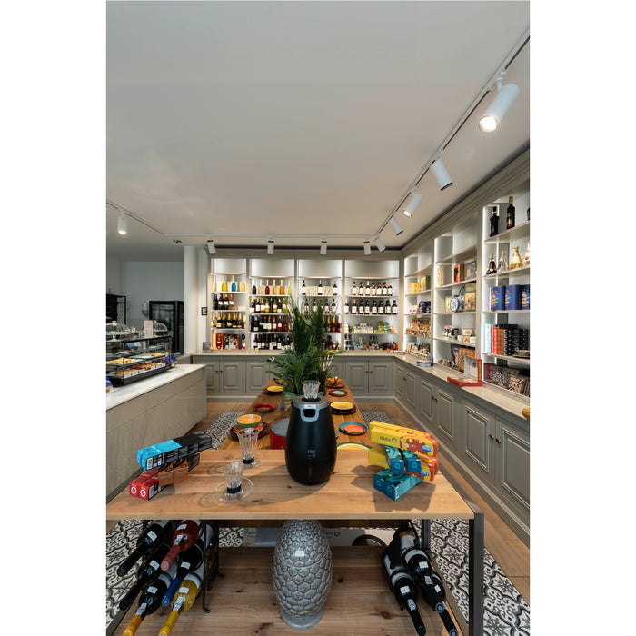 Interior of a shop with a wooden table, grey cabinets, and shelves filled with wine and other products.