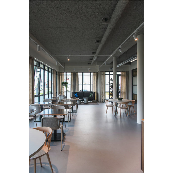 Modern office cafeteria with wood chairs, gray upholstered seating, and large windows.