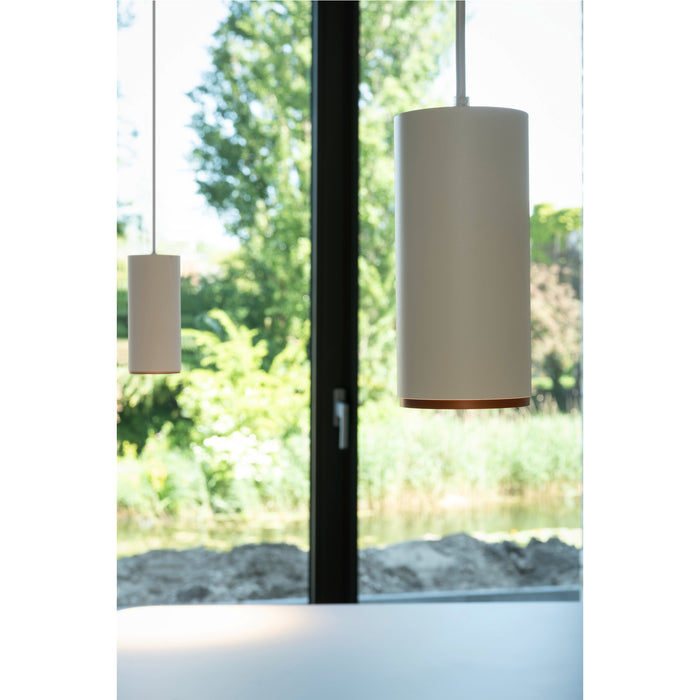 White cylindrical pendant lights with copper accents, suspended in front of a window.