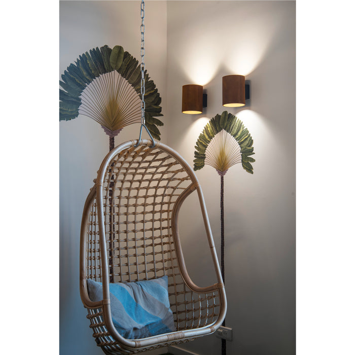 Wicker hanging chair with blue striped pillow, suspended by chain. Wall-mounted brown sconces in background.