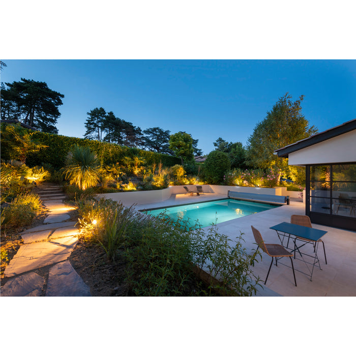 Backyard pool with stone path, landscape lighting, and outdoor dining set.