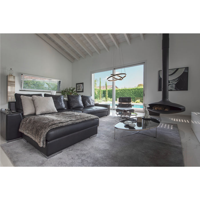 Modern living room with black leather sectional sofa, gray rug, and suspended black fireplace.
