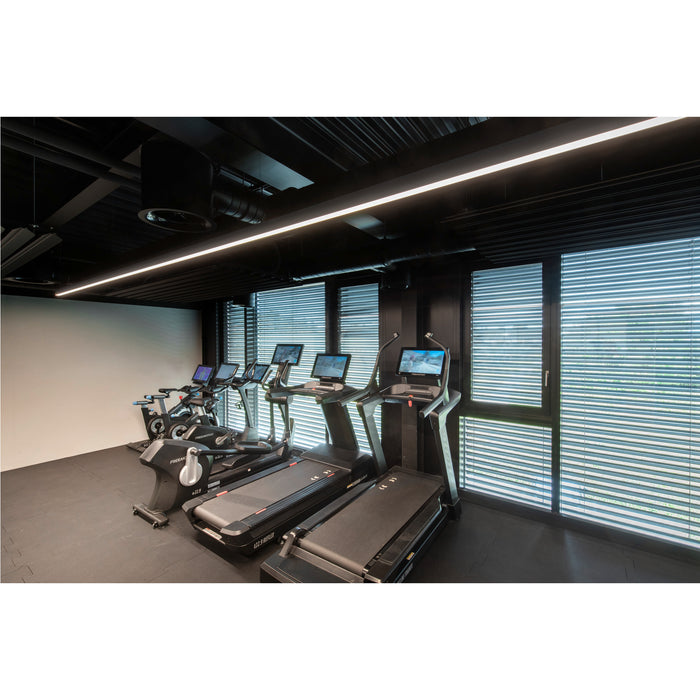 Gym interior with black treadmills and exercise bikes near window blinds.