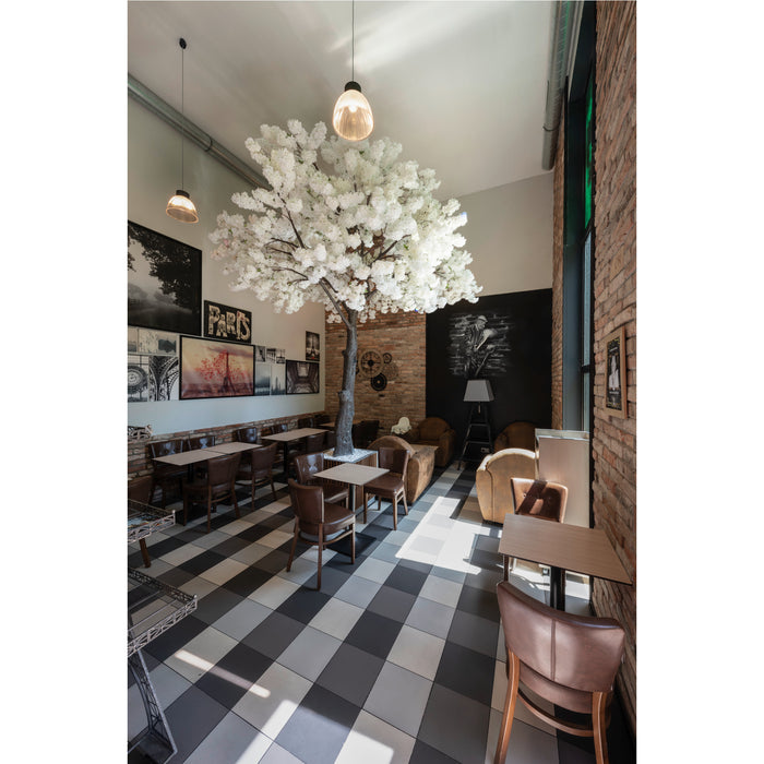 Cafe interior with brown leather chairs, wood tables, black and white tile floor, and a large white artificial cherry blossom tree.