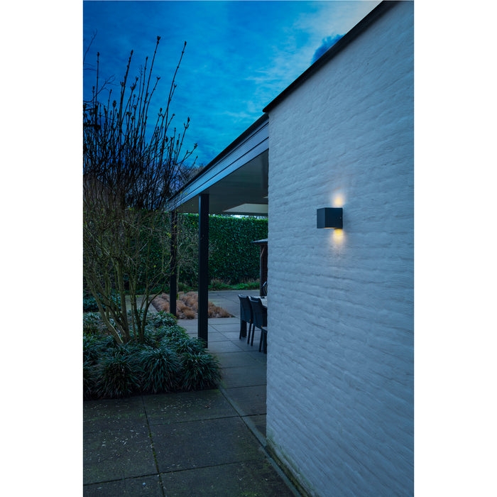 Black cube outdoor wall light, mounted on white brick.