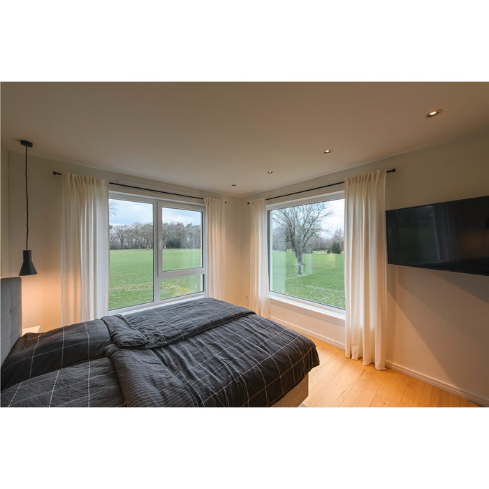 Bedroom with gray plaid bedding, white curtains, and large windows overlooking a green field.