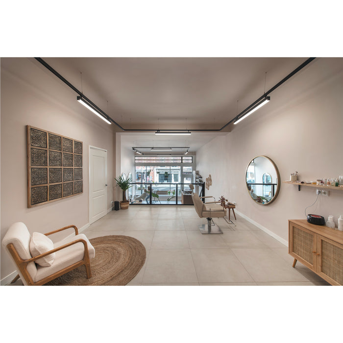 Salon interior with beige walls, tile floor, wood furniture, jute rug, and black track lighting.