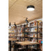 Black cylinder surface-mounted ceiling light fixture in a liquor store with wood slat ceiling and shelves of bottles.