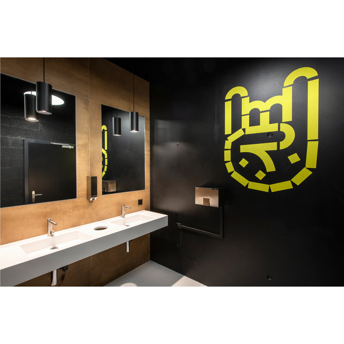 Modern bathroom with white trough sink, stainless steel faucets, black pendant lights, and yellow graphic on black wall.