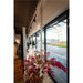 Bridal shop interior with wedding dresses on mannequins, floral arrangement in metallic vase, and black framed windows.