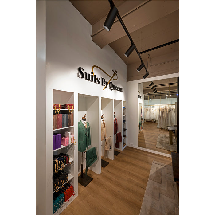 Suits By Queens store interior with suits on display in green, tan, and burgundy, plus dresses visible in a mirror.