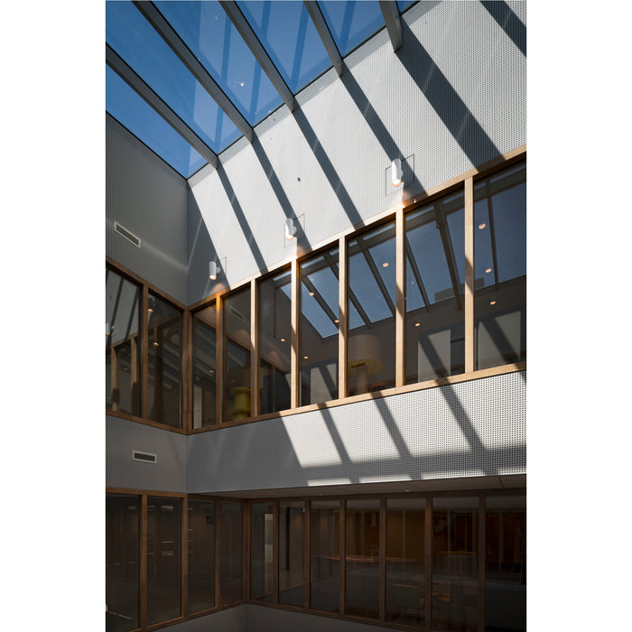 Interior atrium with glass skylight, wood frame windows, and perforated white metal panels.