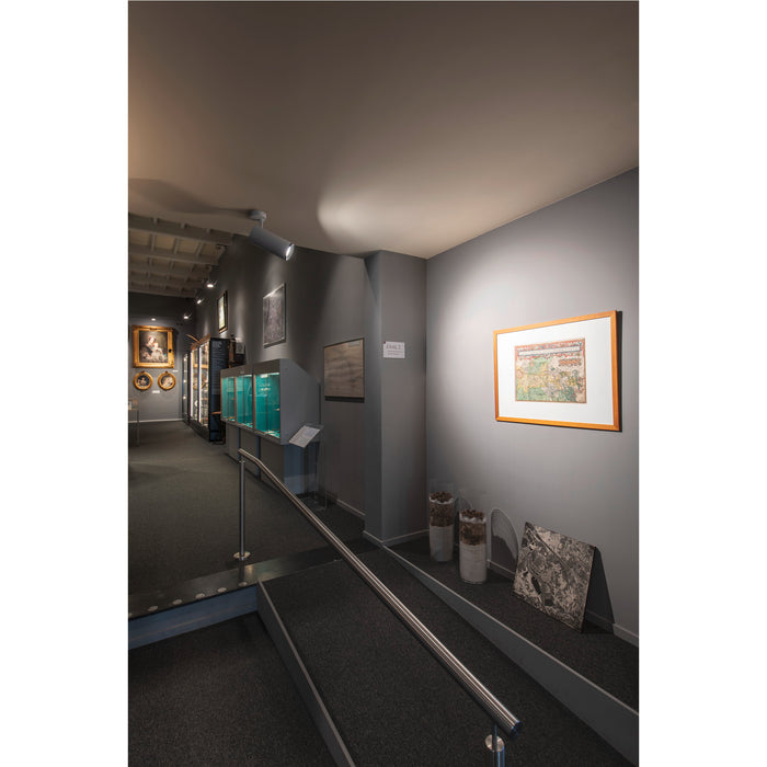 Museum interior with framed map art on gray walls, glass display cases, and a carpeted ramp with a stainless steel handrail.